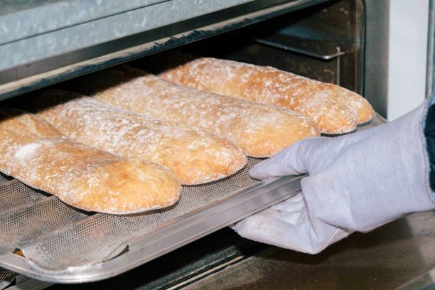 面包师用手套把面包从烤箱里拿出来。图片下载