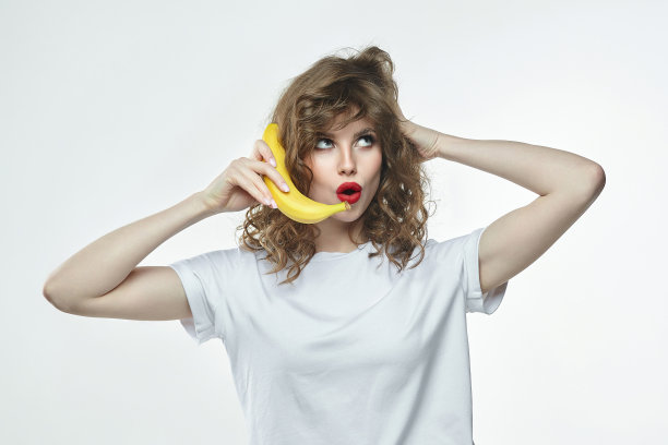 一个漂亮的女孩手里拿着一根香蕉，假装要把它叫过去图片下载