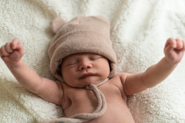 孩子戴着针织帽，没穿衣服，睡在羊毛毯上，举起双手图片下载