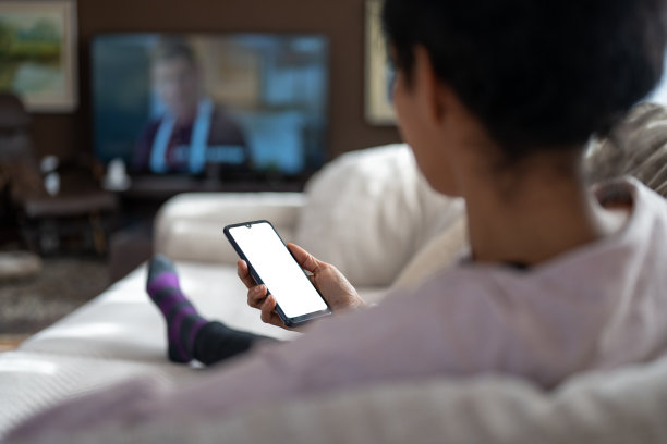 西班牙混血女性一边看电视一边用智能手机图片下载