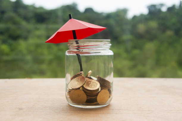小红伞在一堆金币里面的一个坛子在木桌上。金融安全投资理念。图片下载
