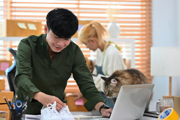 一名微笑的亚洲男子的肖像，电子商务员工站在办公室的包裹在后台工作的笔记本电脑和产品，中小企业业务，电子商务和快递业务。图片下载