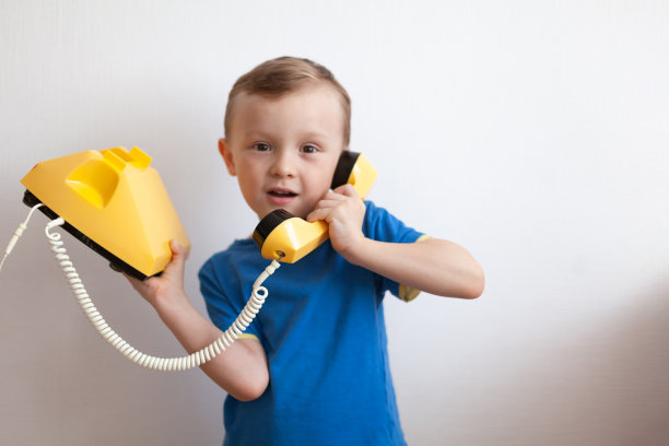 身穿蓝色t恤的4岁男孩正在白色背景的黄色复古手机上聊天图片下载