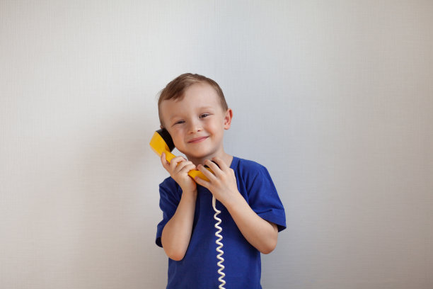 身穿蓝色t恤的4岁男孩正在白色背景的黄色复古手机上聊天图片下载