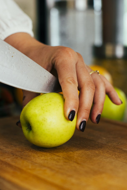 女人准备在砧板上把青苹果切成两半。手，脚和苹果的特写。健康生活，健康饮食。有机食品。股票的照片。图片下载