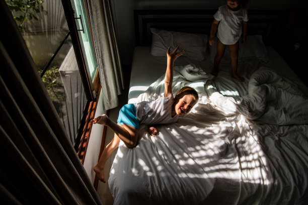 孩子们早上醒得很早。小孩子们在阳光下的床上玩耍跳跃。兄弟姐妹早上在卧室里玩耍图片下载