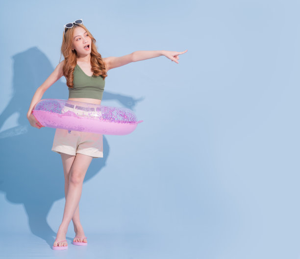 年轻的亚洲女孩抱着游泳浮在蓝色背景，暑假的概念图片下载