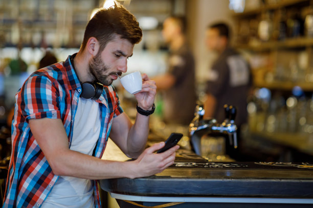 英俊的年轻白人男子坐在咖啡馆使用手机和喝咖啡。图片下载