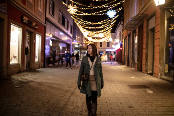 年轻女子在温暖的衣服看向别处，而在城市街道上走在晚上图片下载