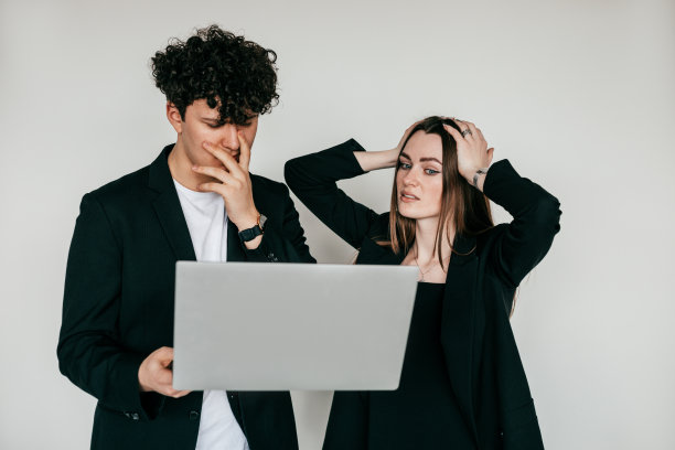 情绪激动的夫妇摆着现代笔记本电脑，穿着优雅的黑色夹克和配件的男人和女人，白色背景。商务人士服装、电子产品的时尚款式目录图片下载