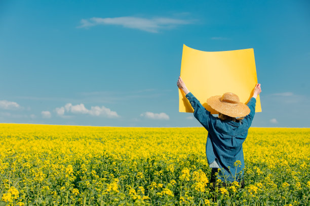 油菜籽田里拿着黄纸的女人图片下载