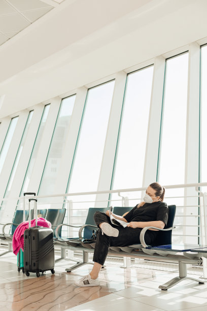 垂直的金发疲惫，无聊的女人戴着医疗口罩，带着行李坐在机场候机楼，等待航班图片下载
