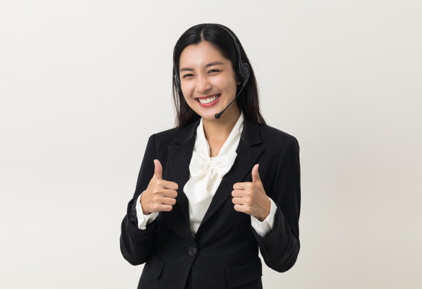 快乐的年轻亚洲商业女性呼叫中心竖起大拇指。欢迎女接线员站在孤立的白色背景上，戴上闲聊耳机。图片下载