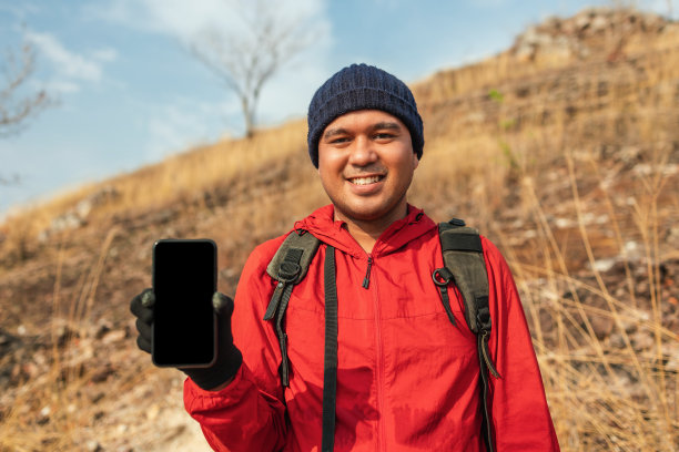 男人旅行者拿着智能手机在假期冒险旅行。背包客站在山顶展示手机。图片下载