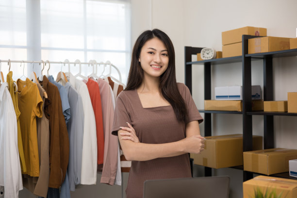快乐年轻美丽的亚洲女人在时尚商店企业主检查库存轨道服装站立和微笑。在服装店工作的亚洲女性企业家。图片下载