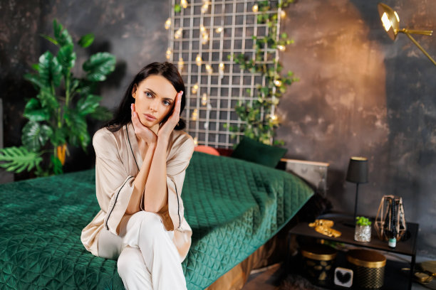 穿着睡衣的女人坐在家里卧室的床上。图片下载