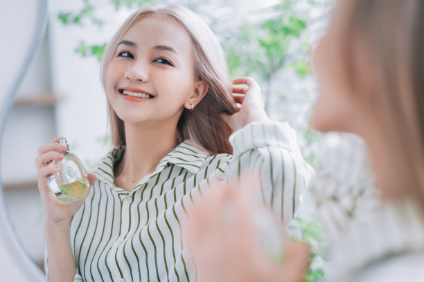 年轻的亚洲女子在镜子前喷洒香水图片下载