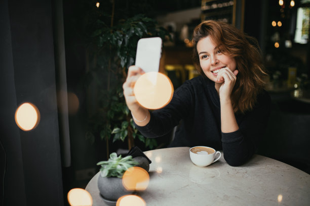 一名年轻女子坐在咖啡馆里喝着咖啡，用着智能手机。图片下载
