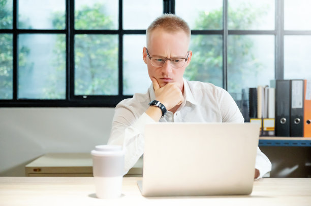 年轻的商人在办公室认真地用笔记本电脑工作。他在思考如何解决工作中的问题图片下载