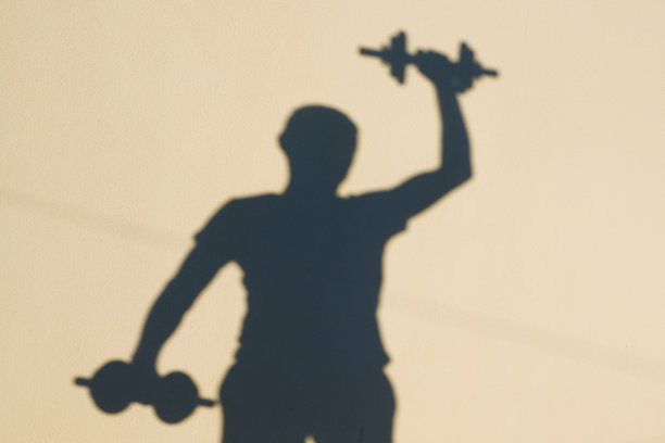 照片中有一个男性的影子。体育的概念。一个男人把哑铃举过头顶。图片下载