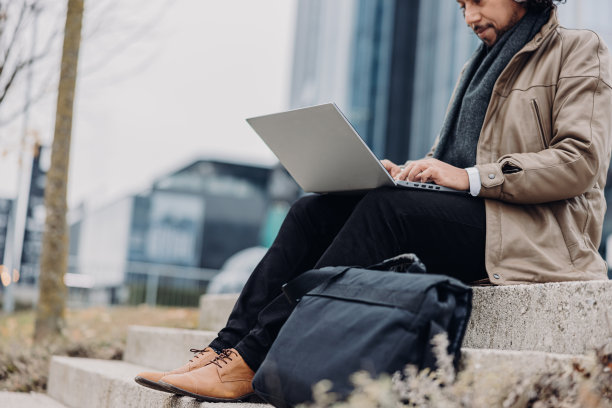 一名商人坐在办公楼前的楼梯上，用笔记本电脑工作图片下载