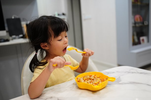 亚洲小女孩自己吃自己坐在餐桌上吃自己的炒饭用黄色的衬衫和黄色的盘子一套勺子和叉子。图片下载