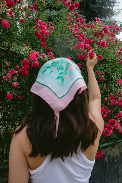 年轻漂亮的女人在盛开的红玫瑰灌木丛旁微笑图片下载