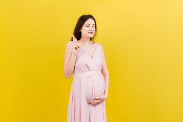 欢快的年轻孕妇双手交叉手指，等待怀孕隔离在彩色背景在工作室。怀孕的生活概念图片下载