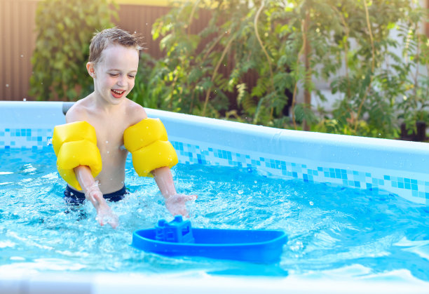 孩子们在户外游泳池玩耍。夏天的花园里，小男孩在自家的游泳池里玩船。图片下载