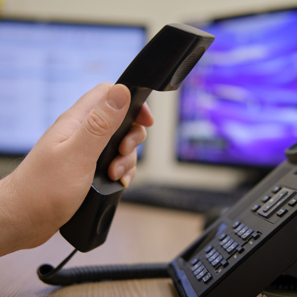 一个男人在办公室电脑的显示器旁拿着一个电话。在工作场所，近距离的办公桌上开始电话交谈图片下载