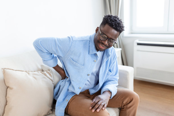 不快乐的人在家背疼。下背部疼痛。男人按摩酸痛的肌肉时感到背部疼痛，悲伤的男人患有腰背疼痛图片下载