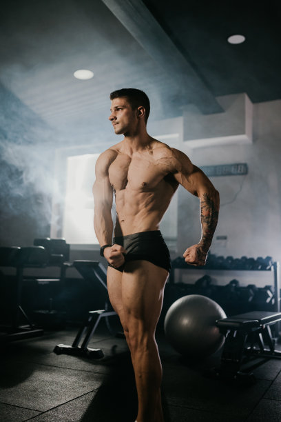 自信的健美运动员，光着上身，一边看健身房一边秀肌肉图片下载