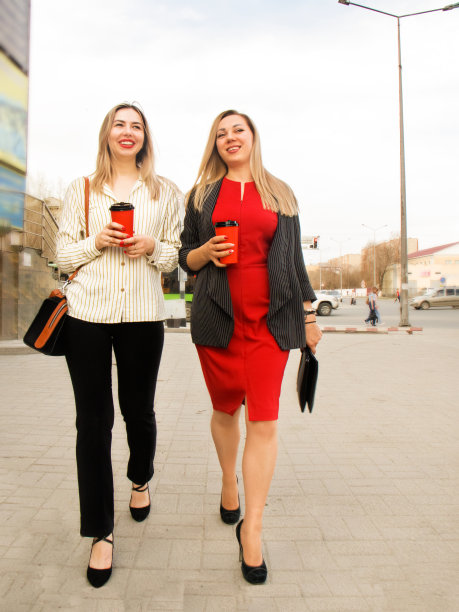 两位商务女性手拿咖啡走在城市街道上交谈图片下载