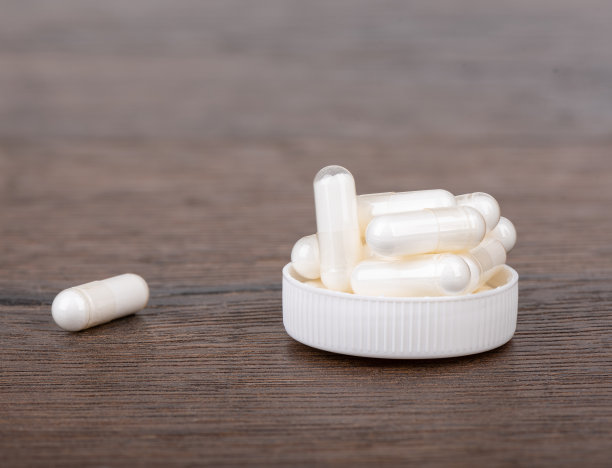 含有维生素D3或膳食补充剂的胶囊，在一个帽和木制背景上。图片下载