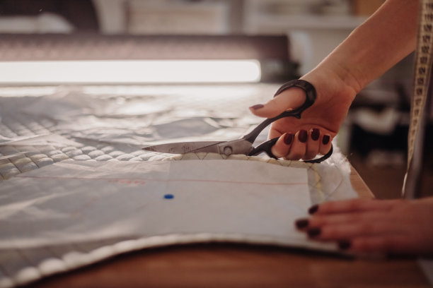 年轻的女裁缝手在车间的桌子上用剪刀剪布图片下载