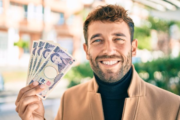 英俊的商人穿着优雅的夹克，在户外开心地微笑着，展示着5000日元的钞票图片下载