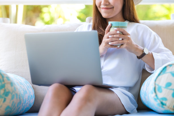 一名年轻女子坐在秋千沙发上喝着咖啡，用笔记本电脑进行远程工作或在线学习的特写画面图片下载