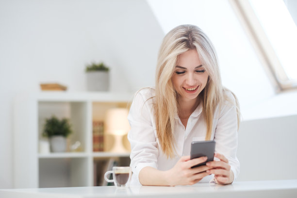 一位年轻美丽的白种人金发女子在家里休息。一个女人坐在桌旁，喝着杯子里的咖啡，读着杂志。图片下载