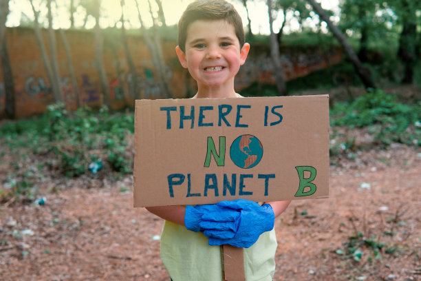 一个英俊微笑的小男孩穿着黄色t恤，戴着蓝色手套，手里拿着一个纸板牌子，上面画着地球的标志，上面写着生态意识的信息图片下载