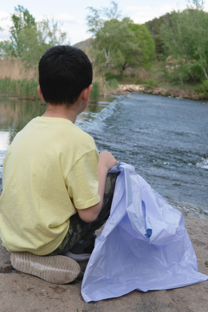 一个男孩坐在大坝的岸上，手里拿着一个垃圾袋。图片下载