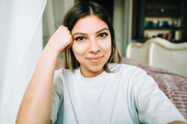 迷人的白人年轻女子的肖像坐在地板上靠近床，看着相机。图片下载