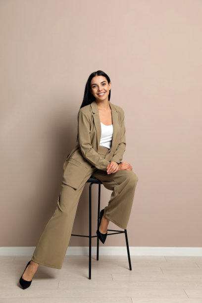 漂亮的年轻女商人坐在米色墙壁附近的凳子上图片下载
