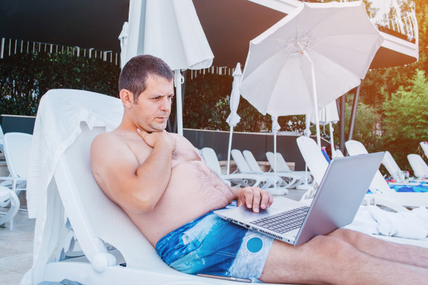 户外工作：自由职业概念。一名在度假的男子在泳池边用电脑工作，在假期中休息和工作。在假期中远程工作，在海滩上用笔记本电脑工作的自由职业者。科技与旅行图片下载