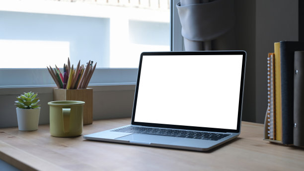 白色屏幕的笔记本电脑，咖啡杯和文具放在木桌上。图片下载