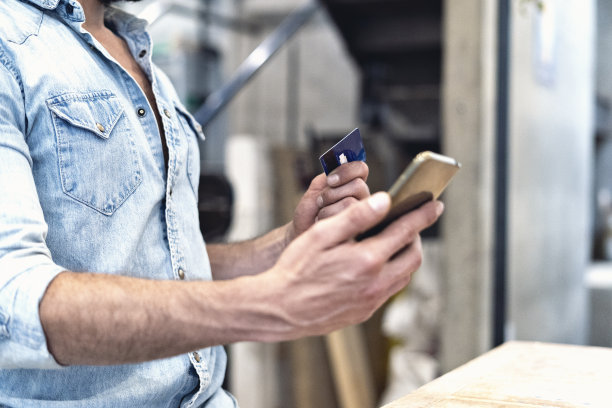 木匠在木工店里，手里拿着手机和一张卡片。图片下载