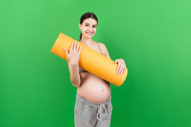 抱着瑜伽垫的怀孕女孩站在彩色背景上。工作室拍摄，设计的自由空间图片下载