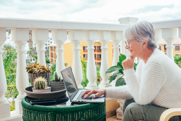 微笑的商业年老妇女打字在笔记本电脑工作从家庭阳台-远程工作的概念图片下载