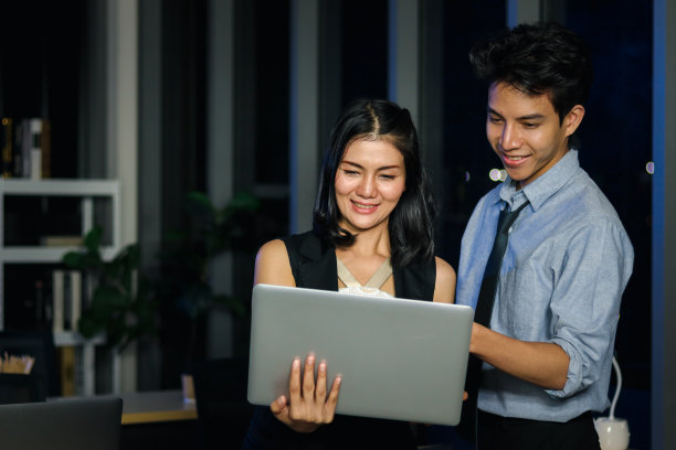 快乐微笑的年轻亚洲男女团队成员在办公室里加班，用笔记本电脑在午夜讨论工作，努力工作，夜班商务人士图片下载