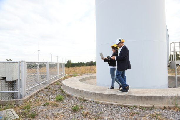 肖像男性和女性维护同事与安全PPE工作在风力涡轮机农场，可再生和绿色能源的概念图片下载