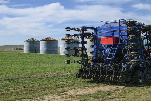 播种机双臂交叉地停在有筒仓、牧场和蓝天的乡村景观中。copy-space图片下载